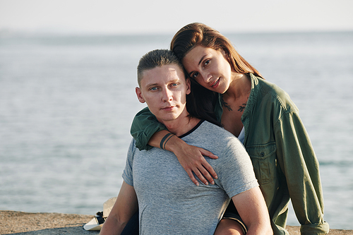 Horizontal medium portrait of young Caucasian man and woman spending time on beach, woman hugging man with one hand