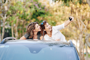 Beautiful happy female friends riding in back of pickup truck and taking selfie on smartphone