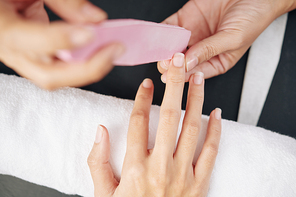 Close-up image of manicurist filing nails of female client, selective focus