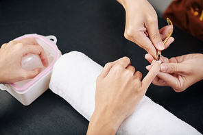 Close-up image of manicurist cutting cuticle on hand of female client, view from above