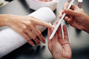 Process of manicurist filing nails of female client, view from above