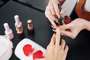 Close-up image of professional manicurist applying classic red nail polish