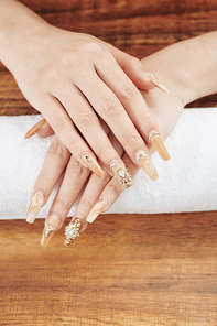 Female hands with fancy beige manicure with rhinestones and beads, view from above