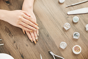 Hands of woman with fancy golden manicure and small containers with beads and rhinestones, view from above