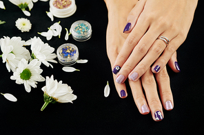 Female hands with dark purple and silver nail design and small containers with beads and rhinestones