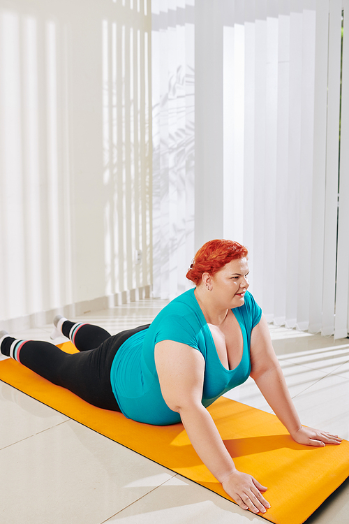Overweight young woman in sports clothes practicing yoga at home