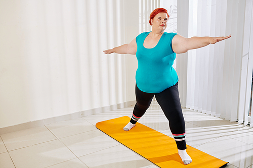 Overweight young woman practicing asana on yoga mat at home