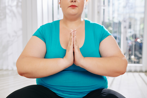 Cropped image of meditating overweight young woman keeping hands in namaste gesture