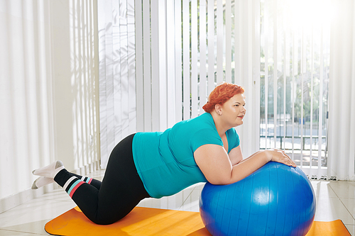 Overweight young woman doing exercises with fitness ball at fitness class in health club