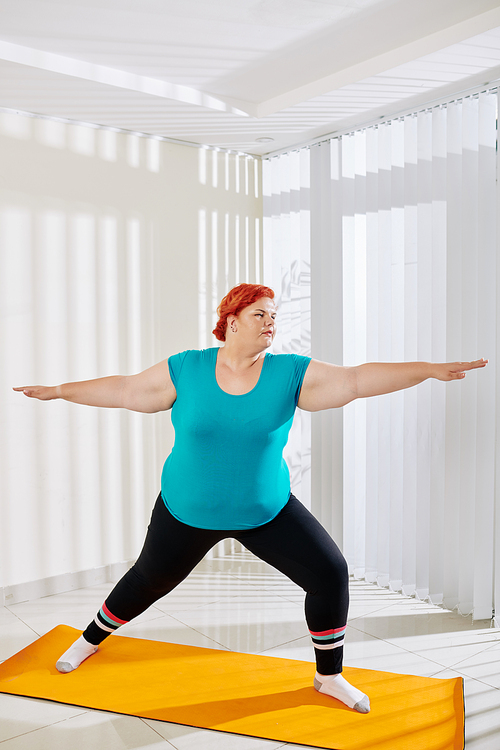 Woman in sports clothes practicing warrior asana in yoga class