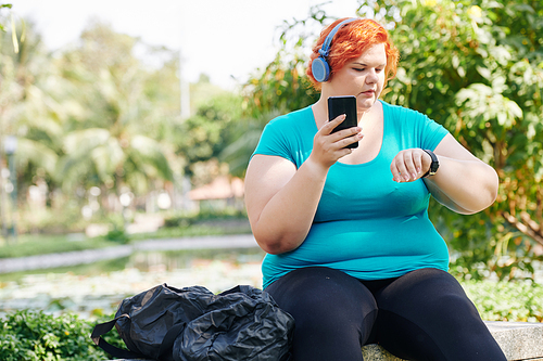 Overweight young woman checking data in her fitness tracker after exercising in city park