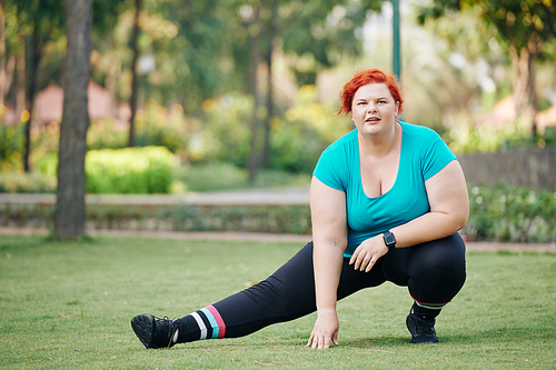 Overweight young woman stretching legs and warming up before training in park