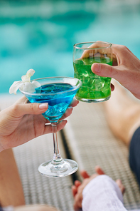 Couple clinking glasses with sweet colorful cocktails when resting by swimming poole