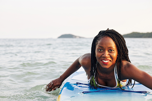 Excited smiling pretty young Black woman swimming on sup board in sea