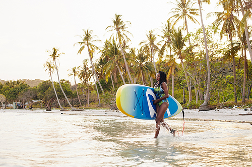 Beautiful happy fit young Black woman with sup board running into sea