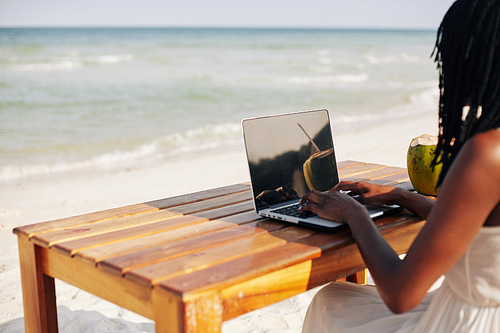 female freelancer or Vlogger sitting at table on the beautiful beach and working on laptop