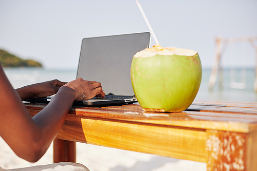 Close-up image of young woman enjoying her vacation on tropical beach, drinking coconut water and checking e-mails