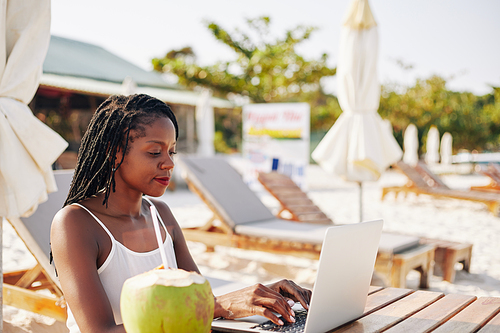 concentrated female vlogger sitting at table on beach and working on article or Vlog post