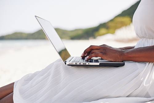 Female freelancer sitting on beach of tropical island and working on laptop