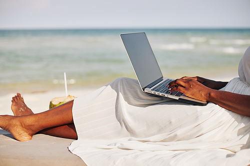 Young woman relaxing on sandy beach and answering subscribers comments on her last video or blog post