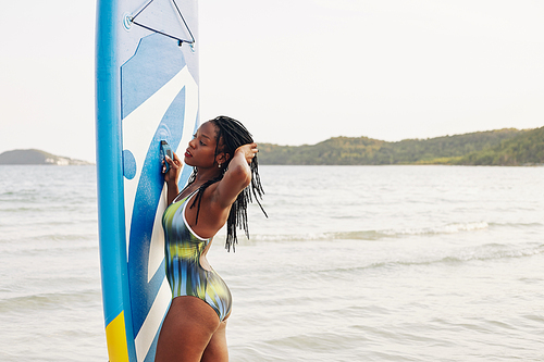 Beautiful sensual young fit woman standing next to sup board and touching her hair