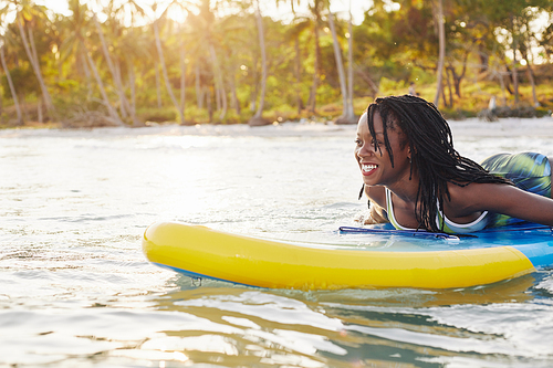 Excited happy young Black woman swimming on sup board in sea when spending vacation on tropical island