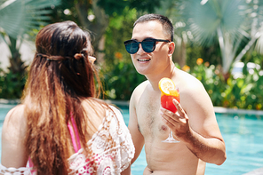 Happy young Asian man spending time in swimming pool with his girlfriend and enjoying delicious fruit cocktails
