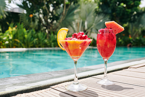Two glasses with red dragon fruit and grapefruit smoothie on edge of swimming pool