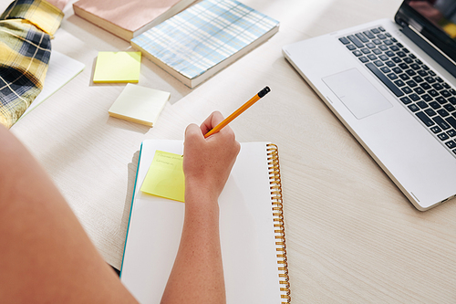 Close-up image of teenae girl writing things she planned to do on sticky notes before starting doing homework at home