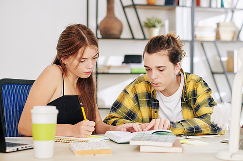 Teenage girl helping classmate with mathematics and explaining him how to solve equations