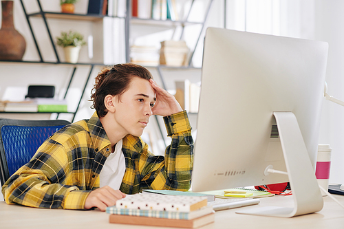 Pensive teenage boy sitting at desk at home when having online class of English language