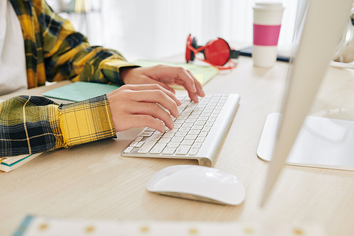 Close-up image of teenager in plaid shirt working on computer at his desk at home