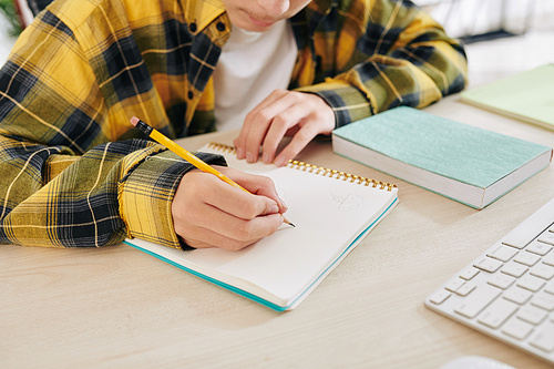 Concentrated teenager making sketches for his school project in notebook