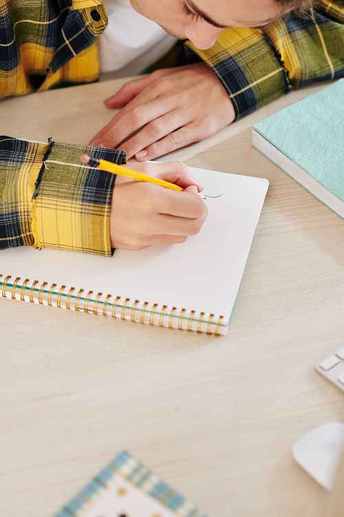 Close-up image of creative teenage boy drawing in notebook when sitting at desk