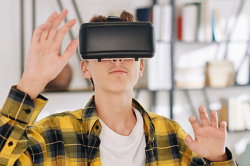 Teenager in plaid shirt playing game in virtual reality headset at home