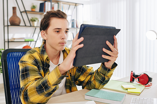 Serious teenage boy watching video, reading article or using application on digital tablet