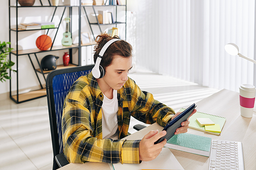 Teenage boy in plaid shirt wearing headphones when watching music video on digital table