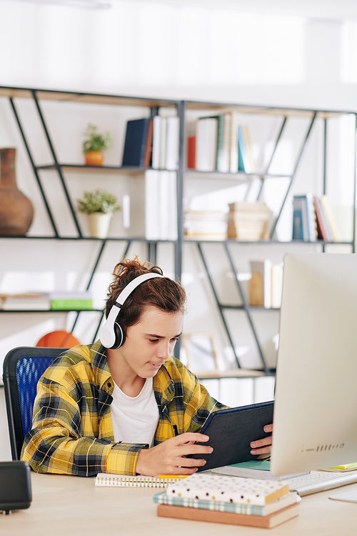 Excited teenager sitting at desk at home and watching television series, blog or music video on digital tablet