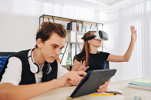 Amazed teenage girl enjoying VR application that her friend controlling via digital tablet