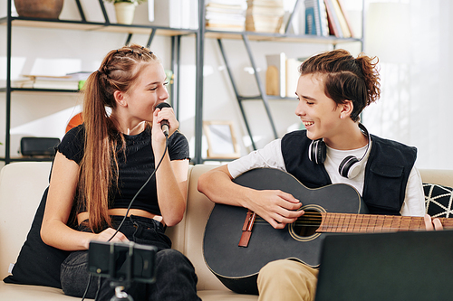 Teenage boy playing guitar when his sister singing song in microphone when recording video on smartphone