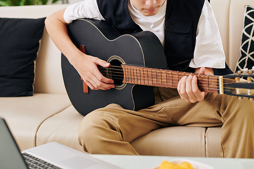 Cropped image of serious teenge boy enjoying playing guitar in front of laptop when streaming on his blog
