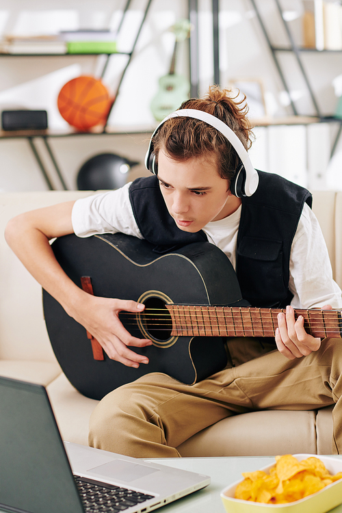 Teenge boy in headphones following chords on laptop screen when learning new song