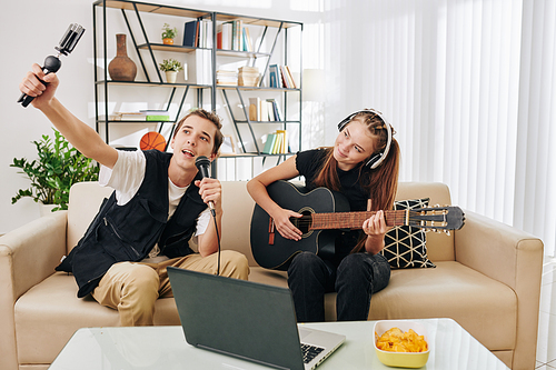 Talented creative teenage couple filming themselves singing and playing guitar
