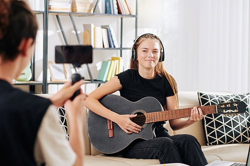 Teenage boy filming his sister singing and playing guitar for blog or contest