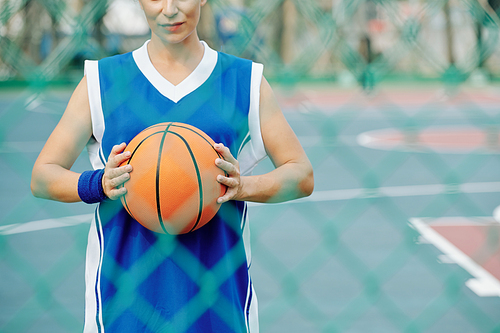 Cropped image of female basketball player standing on outdoor court and holding ball