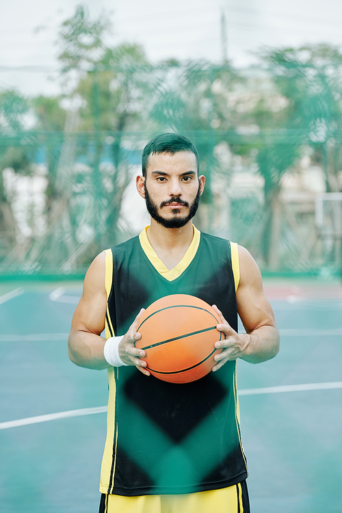 Young handsome serious Hispanic basketball player posing on street basketball court