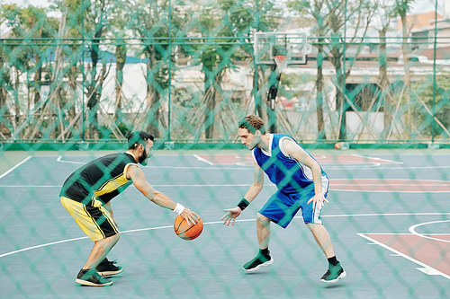 Serious young sportsman playing defense in basketball when training outdoors with friend