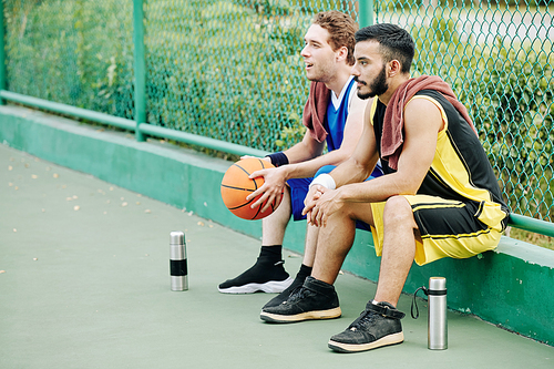 Basketball players having short break and drinking water after playing on outdoor court