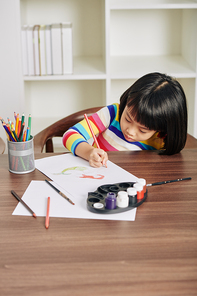 Little Asian girl concentrated on drawing with pencils at desk at home