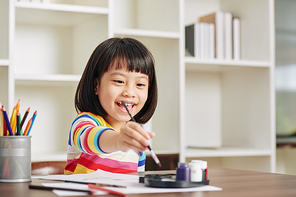Smiling happy cute little Asian girl painting at home